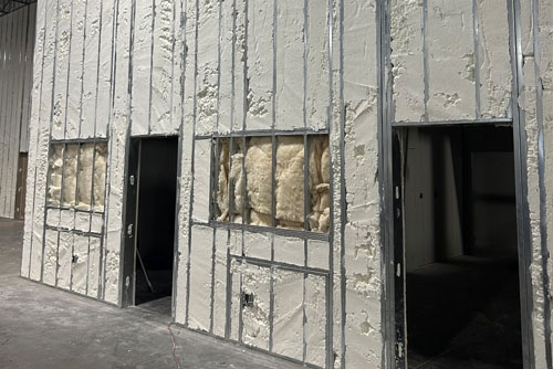 Commercial building under construction with spray foam insulation applied to wall cavities around doors and windows by Woodman Insulation.