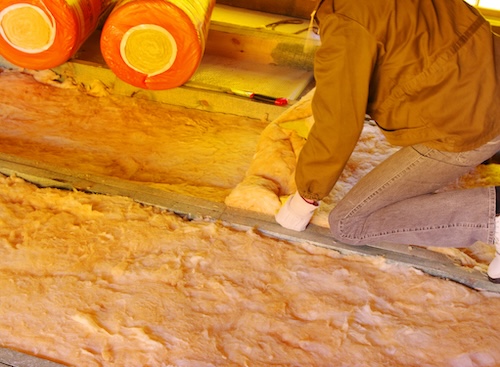 worker laying sheets of insulation between beams