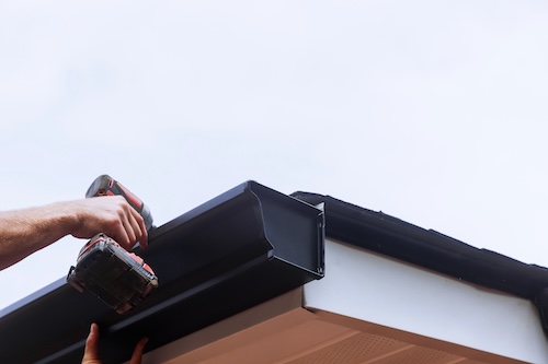 worker drilling new gutters at edge of the roof