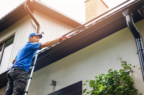 man wearing blue shirt and work gloves standing on ladder while installing gutter guards