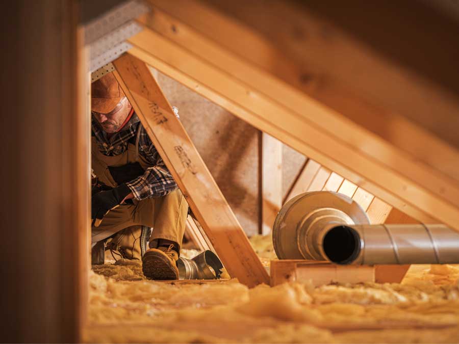 Worker in attic preparing insulation around ductwork.
