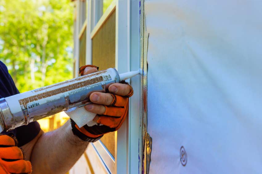 Applying caulk to exterior seams of a house with protective gloves.