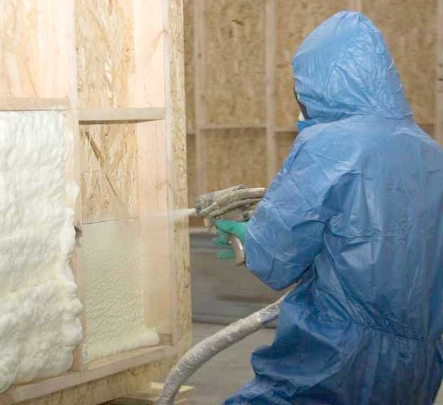 Person applying spray foam insulation wearing blue protective suit.