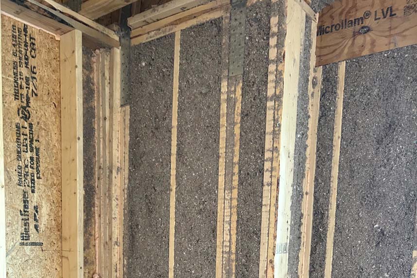 Blown-in cellulose insulation densely packed between wood framing studs inside residential wall under construction