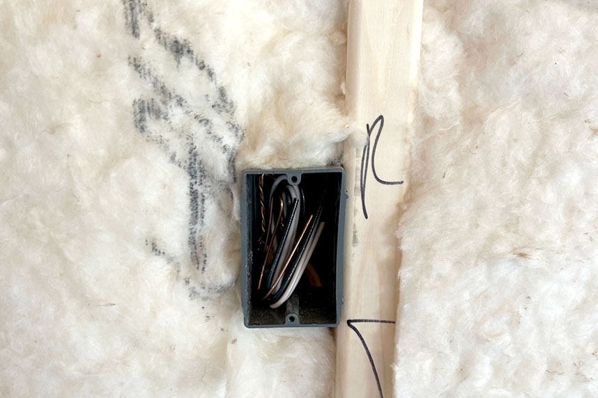 Electrical outlet box installed in a wall cavity surrounded by fiberglass batt insulation.