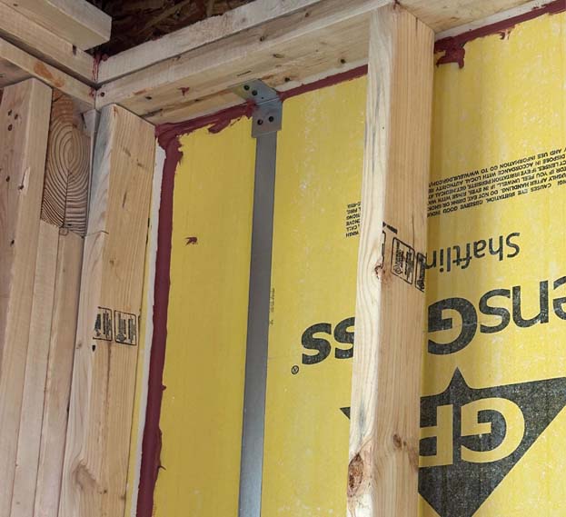 Fire-rated caulk applied at the corner seams of yellow GP sheathing panels in wood framing for code-compliant fire sealing.