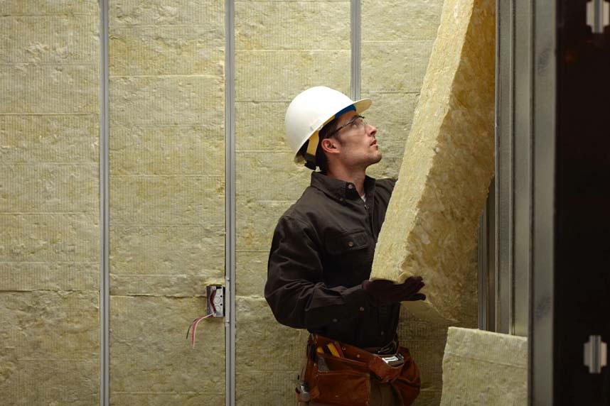 Installer placing rigid mineral wool batt insulation into metal framing for a commercial wall application.