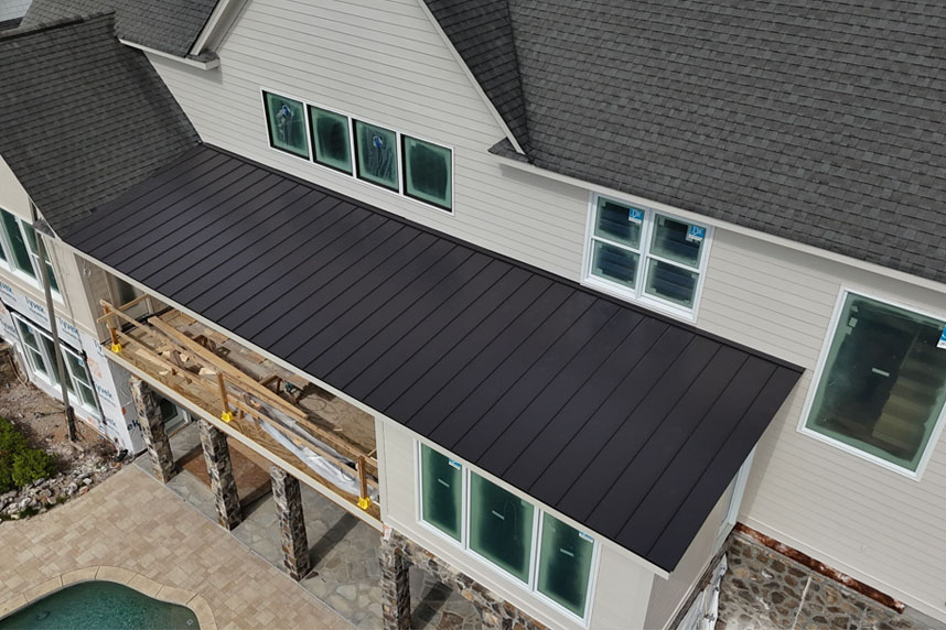 Aerial view of a modern residential home featuring a newly installed black metal porch roof with white siding and large windows.