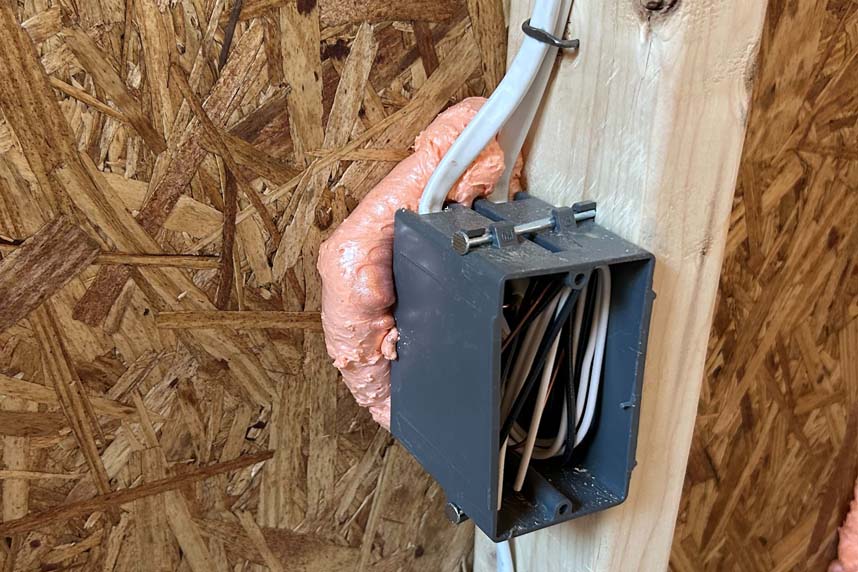 Electrical wiring box mounted to a stud with spray foam sealant applied around wire penetrations to prevent air leakage