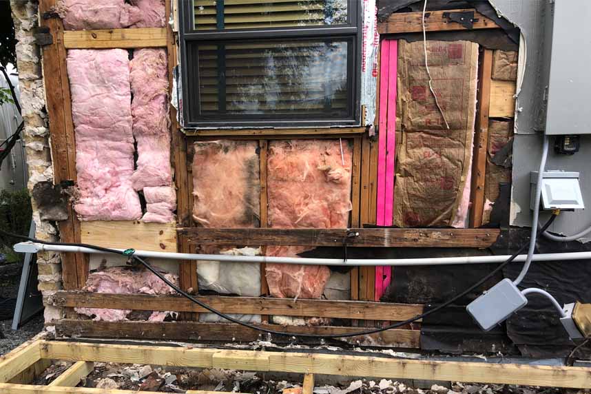Exposed wall cavity showing deteriorated fiberglass insulation and wood framing around a window during home repair.