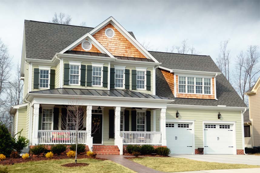 Exterior view of a craftsman-style house showcasing mixed roofing materials, including traditional shingles and modern black metal accents over a white pillared front porch.