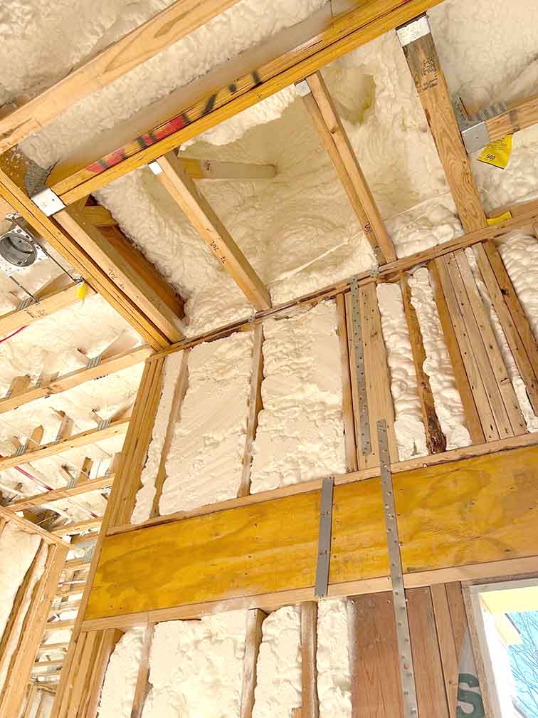 Open-cell spray foam insulation applied to roofline rafters and wall cavity by Woodman Insulation.