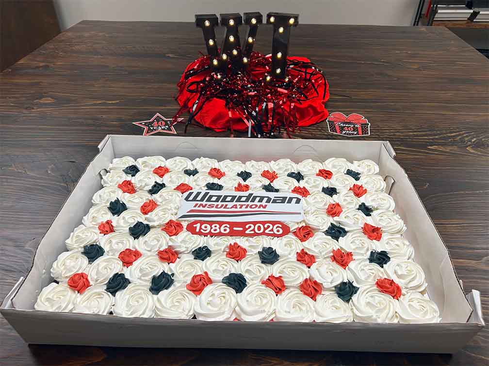 Woodman Insulation 40th anniversary cake decorated with red, black, and white rosettes and a “1986–2026” logo topper, with light-up WI marquee letters.